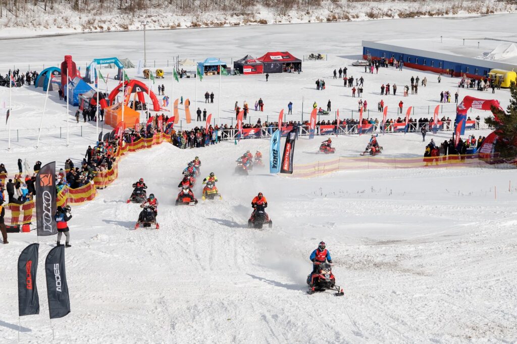 Snowmobiles on the track and spectators by the flags